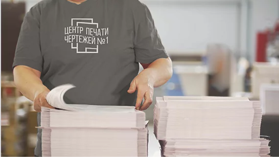 Сотрудник компании Центр печати чертежей №1 укладывает в две стопки печатную продукцию.